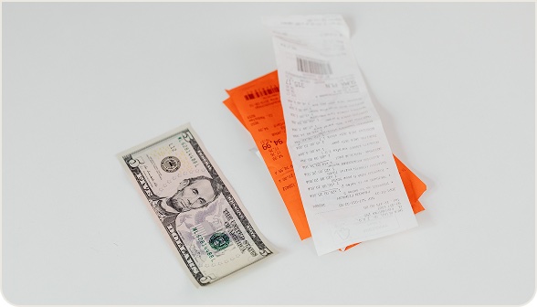 A folded dollar bill next to two paper receipts on a light surface