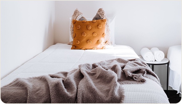 Made bed with a textured orange pillow and folded towels in a short-term rental bedroom