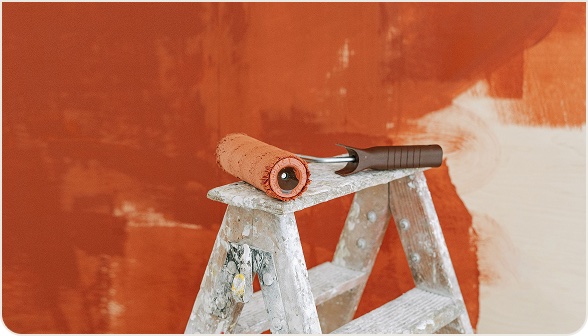 Paint roller resting on a stepladder in front of a half-painted orange wall